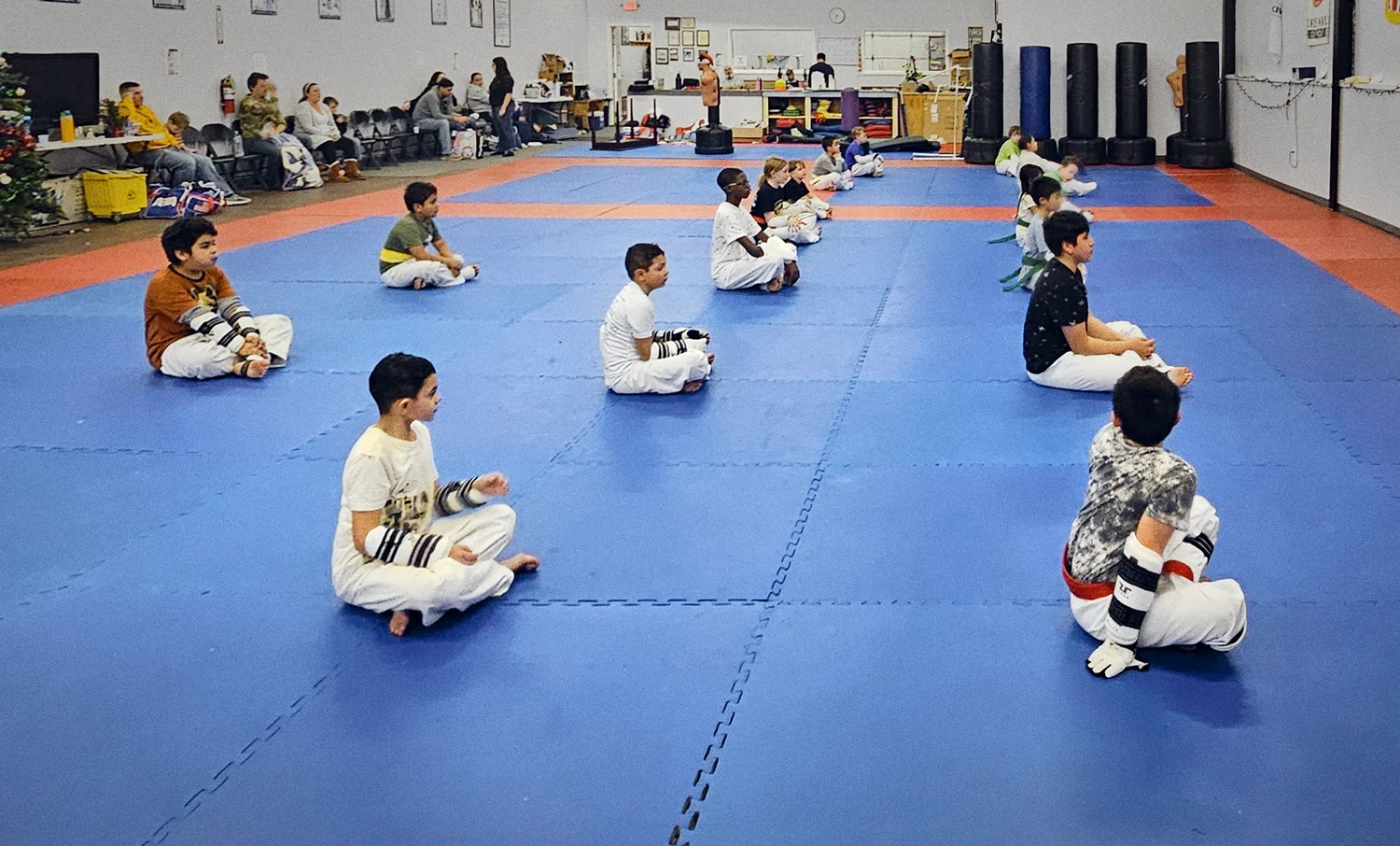 Large group of young students in white gis sitting during Taekwondo class